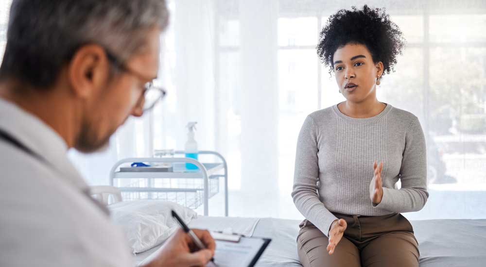 Woman sitting in exam room talking with doctor taking notes
